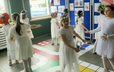 Tańczące dziewczynki w białych, zwiewnych sukienkach, kwiecistych wiankach na głowach.