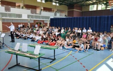 Społeczność szkolna na hali sportowej ogląda koncert zespołu muzycznego.