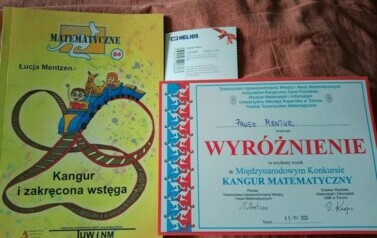 Na zdjęciu widnieje dyplom, książka oraz bilet do kina przyznane uczniowi za wynik w konkursie Kangur Matematyczny.