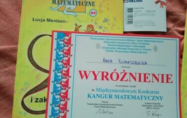 Na zdjęciu widnieje dyplom, książka oraz bilet do kina przyznane uczennicy za wynik w konkursie Kangur Matematyczny