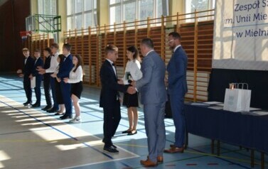 Uczeń klasy &oacute;smej odbiera świadectwo ukończenia szkoły podstawowej od dyrektora podczas uroczystego zakończenia roku szkolnego.