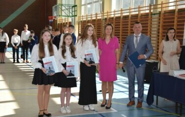 Uczennice klasy sz&oacute;stej, kt&oacute;re otrzymały świadectwa z wyr&oacute;żnieniem pozują do zdjęcia podczas uroczystego zakończenia roku szkolnego wraz z dyrektorem plac&oacute;wki i wychowawcą.