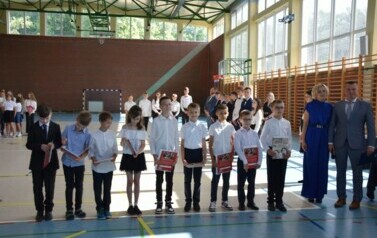 Uczniowie klasy trzeciej, kt&oacute;rzy otrzymali świadectwa za najlepsze wyniki w nauce pozują do zdjęcia podczas uroczystego zakończenia roku szkolnego wraz z dyrektorem plac&oacute;wki i wychowawcą.