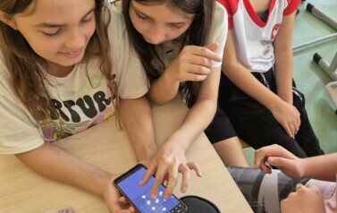 Trzy dziewczynki korzystają wsp&oacute;nie z telefonu kom&oacute;rkowego.