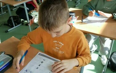 Uczniowie z klasy czwartej siedzą w ławkach szkolnych podczas lekcji matematyki.