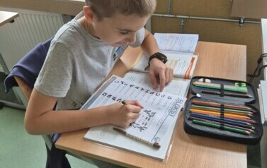 Uczeń siedzi w ławce szkolnej i rozwiązuje zadania matematyczne.