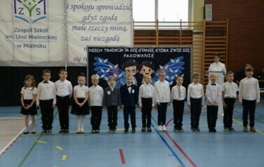 Uczniowie klasy pierwszej, ubrani w galowe stroje, podczas części artystycznej przygotowanej z okazji ślubowania.