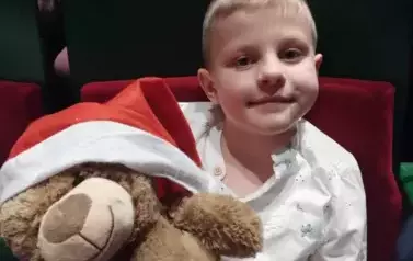 Uśmiechnięty chłopczyk trzyma misia w mikołajowej czapeczce.