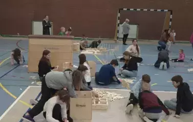 Dzieci układają drewniane klocki rozłożone na hali sportowej
