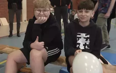Dw&oacute;ch chłopc&oacute;w siedzi na ławce, jeden trzyma biały balon