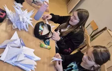Dziewczynki siedzą przy stole i wycinają gwiazdki z gwiałego papieru