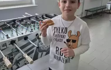 Chłopiec w białej koszulce z czarnymi napisami trzyma pączka