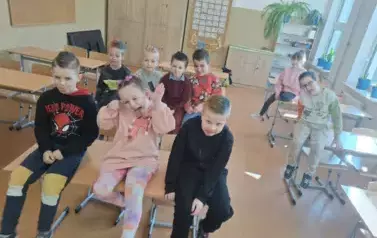 Uczniowie klasy pierwszej siedzą na stolikach w klasie