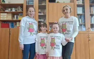 Dwie kobiety i dwie dziewczynki w jednakowych białych koszulkach z czarnymi napisami i rysunkiem żaby