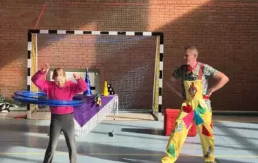 Dziewczynka kręci hula hop. Obok stoi mężczyzna w roku klauna