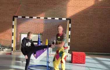 Chłopiec kręci hula hop nogą. Pomaga mężczyzna w kolorowym stroju