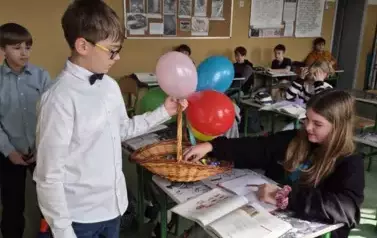 Chłopiec częstuje cukierkami dziewczynkę siedzącą w ławce szkolnej