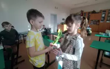 Chłopiec wręcza kwiatek dziewczynce w kucykach, białej bluzce i sukience