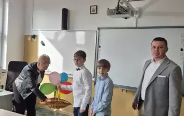 Dw&oacute;ch chłopc&oacute;w i mężczyzna z wiklinowym koszem pełnym cukierk&oacute;w oznobionym kolorowymi balonami