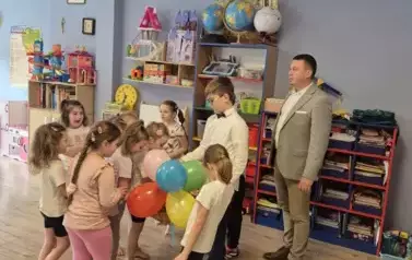 Mężczyzna w graniturze oraz chłopiec w eleganckim stroju częstują cukierkami z okazji Dnia Kobiet grupę dziewczynek z przedszkola