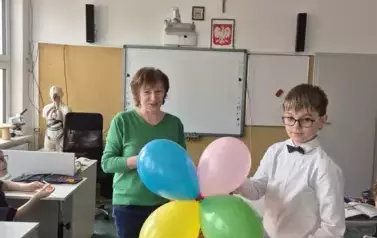 Chłopiec z kolorowymi balonami, obok kobieta w zielonym sweterku i jeansowych spodniach
