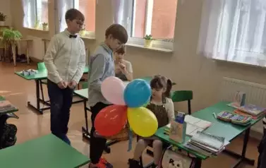 Chłopcy z klasy czwartej, w eleganckich strojach, składają życzenia z okazji Dnia Kobiet dziewczynce z klasy pierwszej