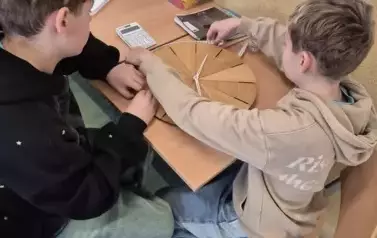 Dw&oacute;ch chłopc&oacute;w mierzy obw&oacute;d drewnianego, okragłego zegarka