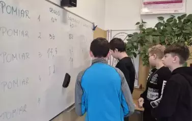Chłopcy stoją przy białej tablicy w sali matematycznej