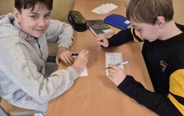 Chłopcy rozwiązują szyfrowankę matematyczną. Jeden z nich usmiecha się do zdjęcia