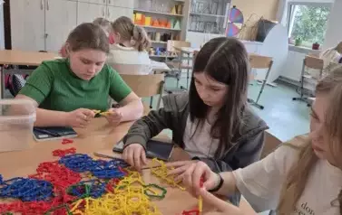 Dziewczynki siedzą przy stoliku, na kt&oacute;rym znajdują się kolorowe klocki w kształcie figur geometrycznych
