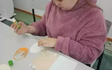 Uczennica siedząca przy stole wykonująca kartkę wielkanocną.