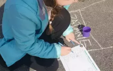 Uczennica pochylona nad kartką i rozwiązująca zadanie matematyczne