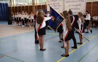 Uczniowie w galowych strojach z przewieszonymi biało-czerwonymi szarfami składają przysięgę na sztandar szkoły