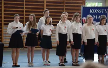 Uczniowie w czarno-białych strojach recytują wiersze podczas uroczystości.