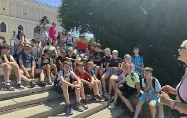 Grupa uczni&oacute;w siedzi na schodach i pozuje do zdjęcia