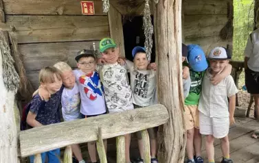 Chłopcy stoją w rzędzie za barierką przed wejściem do starej chatki