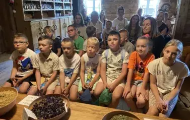 Dzieci siedzą w rzędzie na ławeczce i słuchają