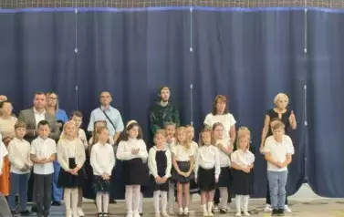 Uczniowie pierwszej klasy ubrani na galowo  stoją w rzędzie