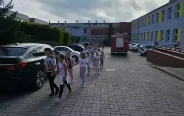 Dzieci z pierwszej klasy idą obok wozu strażackiego.