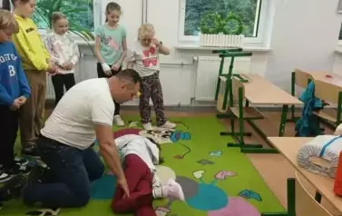 Grupa uczni&oacute;w przygląda się instruktorowi podczas zajęć pierwszej pomocy