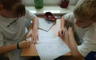 Uczniowie siedzą w ławce i wykonują karty pracy
