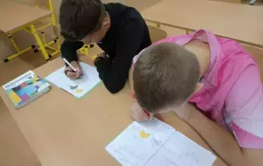 Uczniowie siedzą w ławce i wykonują kartę pracy
