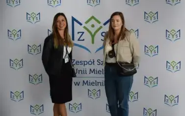 Absolwenci z uśmiehem pozują na tle ścianki
