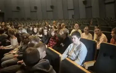 Uczniowie siedzą na krzesełkach i oczekują na rozpoczęcie spektaklu