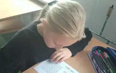 Uczennica siedzi w ławce i rozwiązuje zadanie