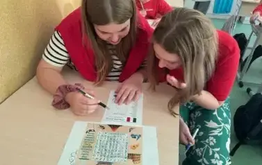 Uczennice ubrane w barwy włoskiej flagi rozwiązuja kartę pracy