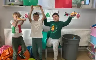 Trzech uczni&oacute;w pozuje na tle flagi Włoch