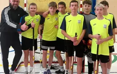 Uczniowie ubrani w stroje sportowe wraz z trenerem pozują do zdjęcia