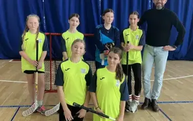Grupa dziewcząt w strojach sportowych pozuje do zdjęcia wraz z trenerem