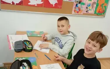 Dw&oacute;ch chłopc&oacute;w siedzi w ławce szkolnej i rozwiązuje labirynt z matematyczną sową